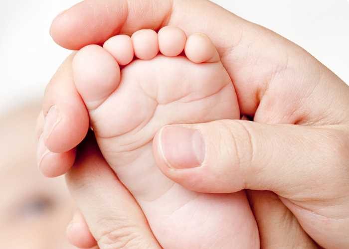 Mãos de adulto segurando com cuidado o pezinho de um bebê